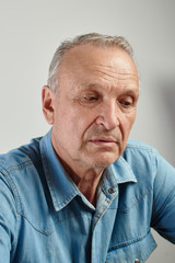 Portrait of serious handsome elderly man with gray hair, stylishly dressed , looking down against white background