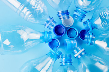 Set of empty different type water bottles lie isolated on blue background, top view. Plastic production and processing concept