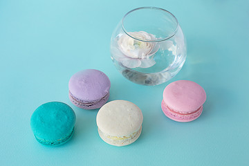 colorful macaroons on a blue textural background with a ranunculus flower in a vase