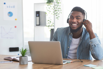 Smiling employee working on laptop and listening music in headphones