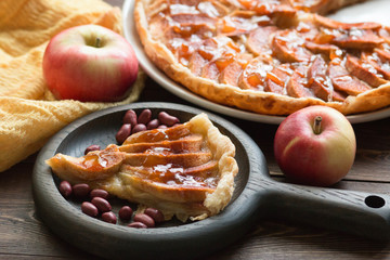 A piece of apple pie with roasted peanuts, fresh apple and caramel sauce on a plate