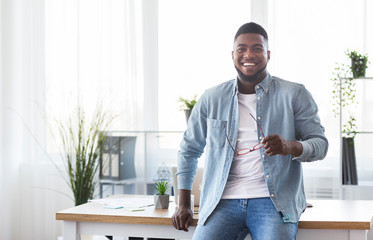 Successful businessman leaning on office desk and looking at camera