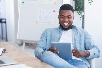 Cheerful african businessman sitting with digital tablet in modern office