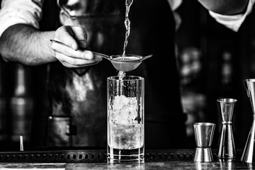 barmen pouring drink through sieve into glass with ice, black_white photo