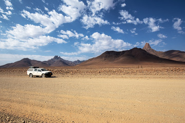 Fototapeta na wymiar off-road vehicle along a desert road in Namibia with beautiful clouds. Africa