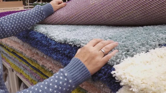 Woman hands choosing a colorful textile carpets in a hardware store in DIY shopping mall.