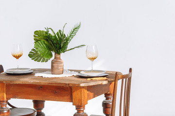 Beautiful wooden table and two chairs in a stylish room with green plants are served for dinner with glasses of wine. Romantic concept