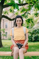 Naklejka premium Happy girl holding digital camera while sitting on bench near university