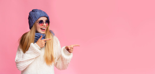 Happy winter girl with sunglasses pointing at empty space