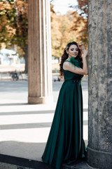 Fototapeta premium Beautiful girl with long wavy hair in green dress. Brunette with curly hairstyle posing. Beautiful woman with professional make up. Sexy girl posing. Female fashion.