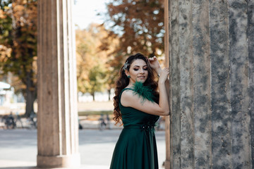 Naklejka premium Portrait of beautiful young girl in green dress. Fashion photo. Beautiful long curly hair woman with closed makeup eyes and manicured nails. Young beautiful stylish girl walking and posing. 