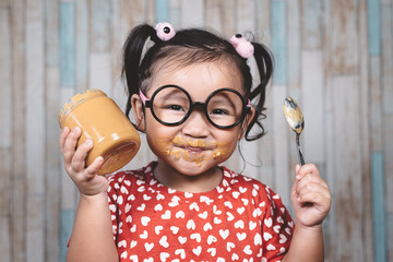 little asian girl holding and enjoying peanut butter in jar and a spoon, Concept of peanut butter lover