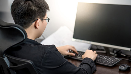 Asian businessman wearing glasses dressed in black working with computer in office. Work routine urban lifestyle. Business and technology concept