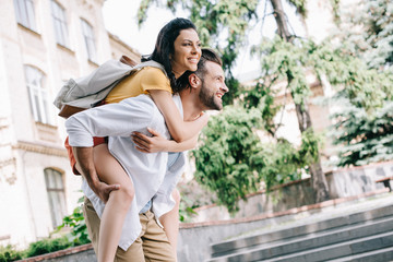 happy bearded man piggybacking girl near building