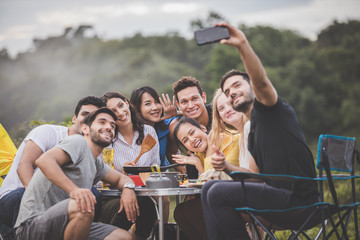 Camping season, Group of campers are having fun talking and taking selfies together with full kitchen equipment on the table. © Sumala