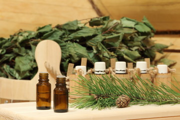 Fototapeta na wymiar Bottles with healing essential oil for sauna near green pine branch. The concept of natural aromatherapy and spa treatment.