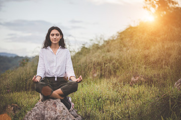 Traveling and camping concept -  Young peaceful woman is enjoying sitting in a yoga pose with a natural forest view.