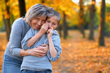 Portrait of mother with her sad daughter in autumn city park. Bright yellow trees and leaves