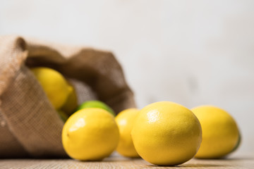 Lemons studio image. Bag of lemons and lime. Fabric bag with lemons. Full sack of lemons on a wooden background.