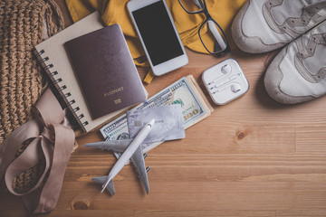 Top view model plane with passport, Yellow hat and smartphone and headphones and bag on a wooden table.