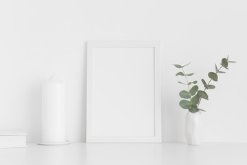 White frame mockup with workspace accessories and eucalyptus in a vase on a white table. Portrait orientation.