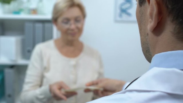 Male therapist giving pharmacological prescription to old female patient, cure