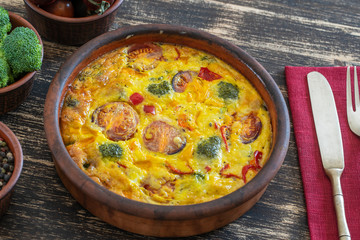 Ceramic bowl with vegetable frittata, simple vegetarian food. Frittata with egg, tomato, pepper, onion, broccoli and cheese on wooden table. Italian egg omelette