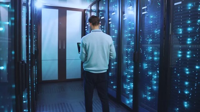 System administrator with notebook checking system of working server racks with supercomputers in modern innovation data center. Render farm. Future technology.
