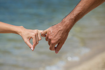 The man and the woman keep for hands. Against the sea water on the beach, close up