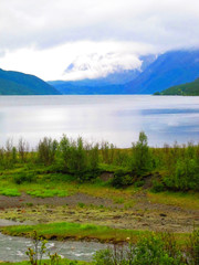 Fjord landscape in Norway. Mountains, tranquil water, low-hanging clouds and verdant shore.