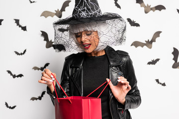 shocked woman in witch hat and wig holding shopping bag in Halloween