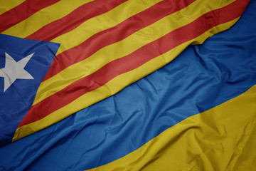 waving colorful flag of ukraine and national flag of catalonia.