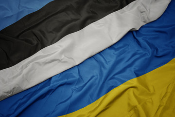 waving colorful flag of ukraine and national flag of estonia.