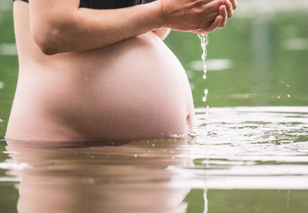Pregnant woman pouring water on her belly bathing outdoor