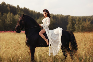 Girl in a long dress riding a horse, a beautiful woman riding a horse in a field in autumn. Country...
