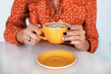 Woman's hands with perfect manicure holding cup of coffee in cafe.