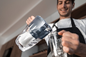 young man pours clean water into a glass
