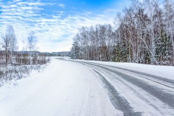 Patterns on the winter highway in the form of four straight lines. Snowy road on the background of snow-covered forest. Winter landscape.