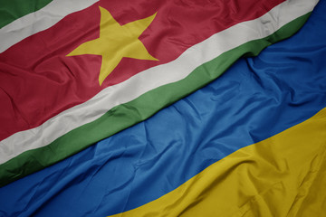 waving colorful flag of ukraine and national flag of suriname.