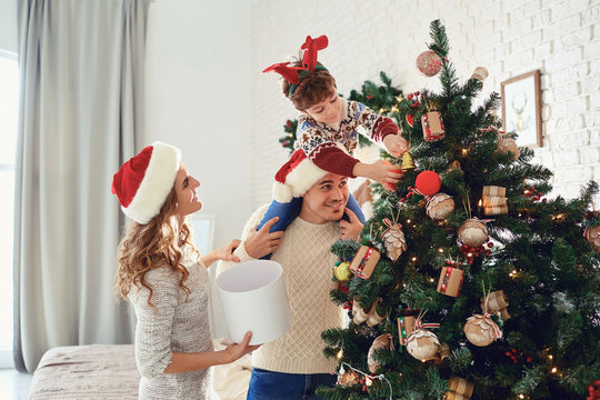Family in sweaters paint the Christmas tree in the house.