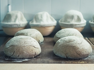 4 loaves of unbaked artisan bread on a wooden griddle with a few baskets for the bread in the background
