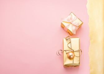 Festive boxes with satin ribbon bow golden toy balls a pastel pink background. Flat layout. Holiday concept. Copy space.