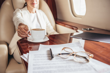 Fototapeta na wymiar cropped view of businesswoman in suit taking cup in private plane