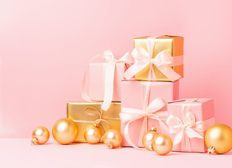 Festive golden pink boxes with satin ribbon bow toy balls on a pastel pink background. Holiday concept. Front view