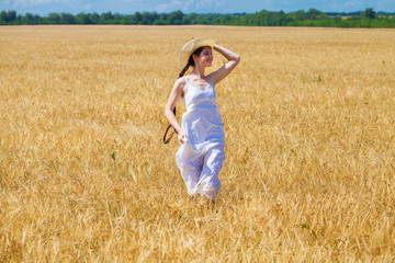 Naklejka na ściany i meble Young brunette woman in white dress walking in a wheat field