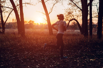 Runner training in autumn park. Woman running with water bottle at sunset. Active lifestyle. Silhouette