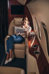 Obraz na płótnie Canvas attractive woman in shirt reading newspaper business in private plane