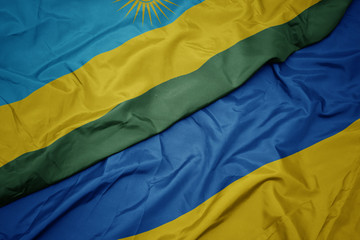 waving colorful flag of ukraine and national flag of rwanda.