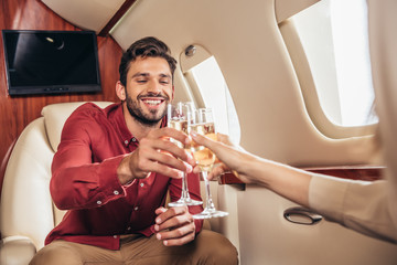 smiling boyfriend and girlfriend clinking with champagne glasses in private plane