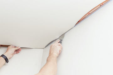 Installing a stretch ceiling in the room. Close up photo of man's hands with a special tool.